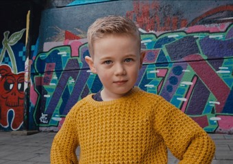 Picture of a child wearing a yellow jumper, standing outside