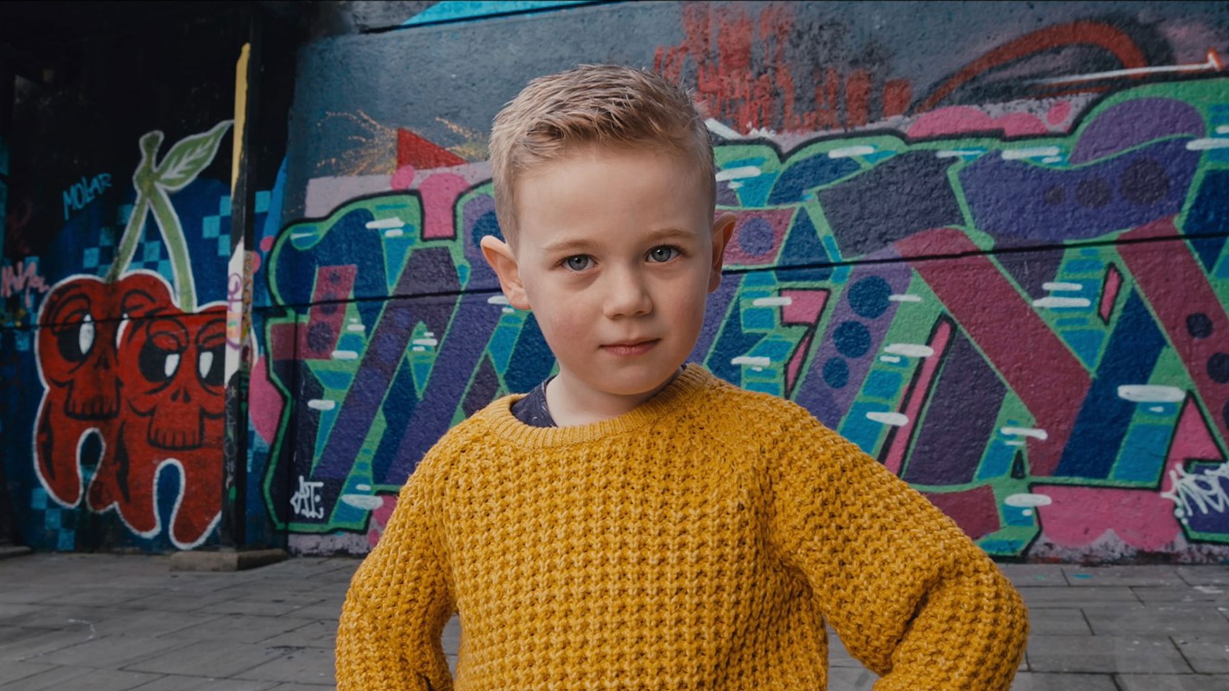 Boy in orange sweater in front of graffiti wall