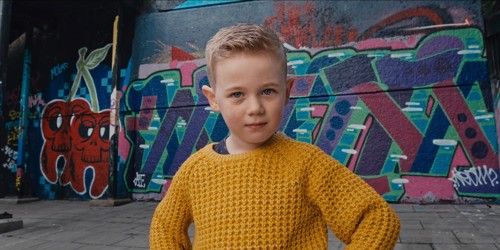 Picture of a child wearing a yellow jumper, standing outside